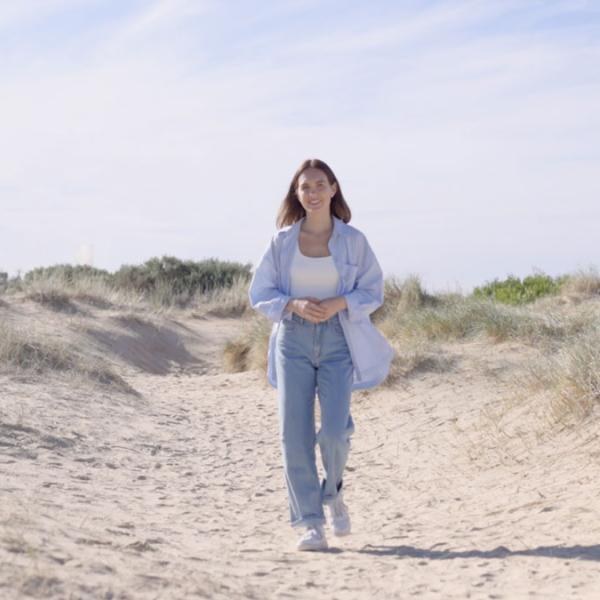 Female in jeans and shirt walking along sand dunes